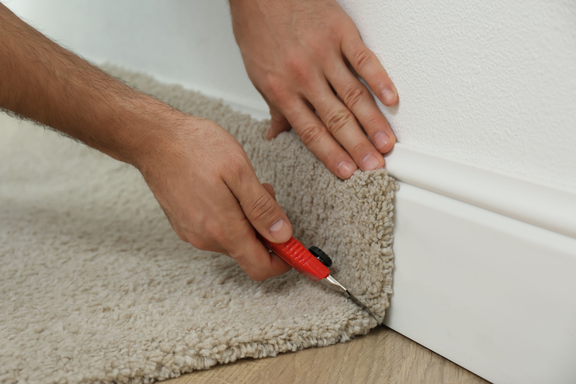 Worker with cutter knife installing new carpet indoors, closeup